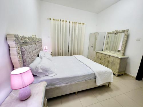 1 dormitorio con 1 cama con lámpara de color rosa y espejo en Cheap Holiday Home, en Ajman
