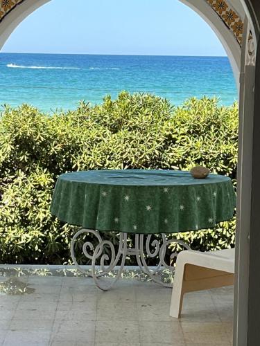 a table with a green table cloth on it with the ocean at Villa De la mer in Rafrāf
