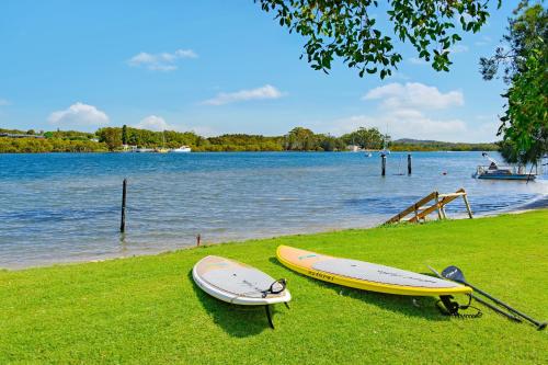 two surfboards sitting on the grass next to a body of water at Punt House - riverfront home with ramp access in Dunbogan