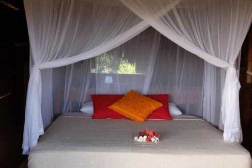 1 cama con almohadas rojas y dosel blanco en Rumah Tinggi at Pachamama, en Nembrala