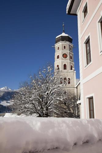 a clock tower with a tree in front of a building at Ferienwohnung Alpblick in Bludenz
