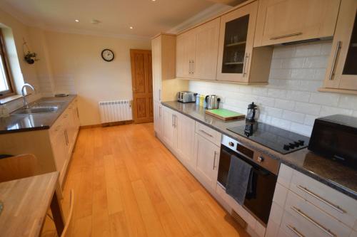 威廉堡的住宿－Gallunach House，厨房铺有木地板,配有白色橱柜。