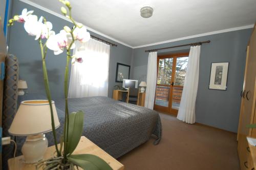 Hotel Des Geneys في باردونيكيا: غرفة نوم مع سرير وطاولة مع مزهرية مع الزهور