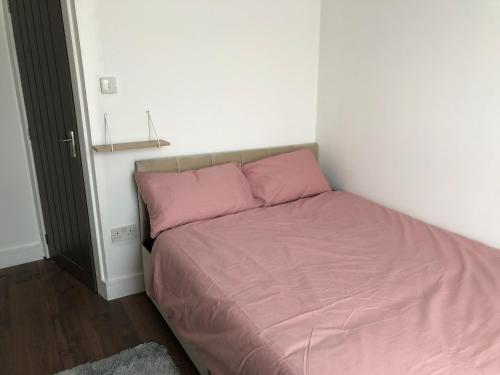 uma cama com lençóis cor-de-rosa num pequeno quarto em Blue house em Lincoln