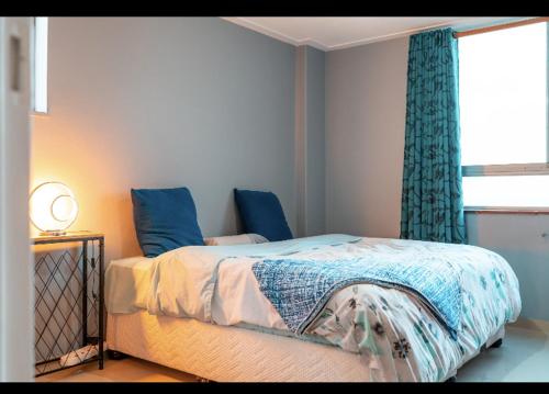 a bedroom with a bed with blue curtains and a window at Mai Paradise in Kingsburgh
