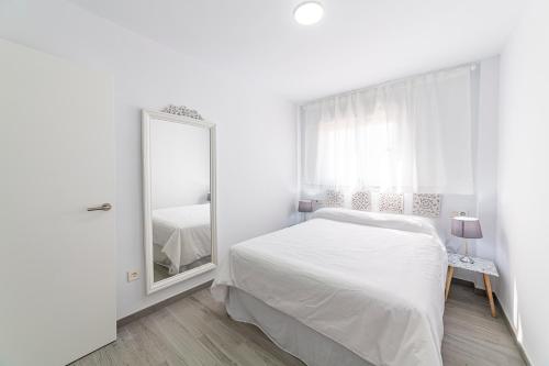 a white bedroom with a bed and a mirror at Apartamentos “Mar de Coral” Aguadulce in Aguadulce