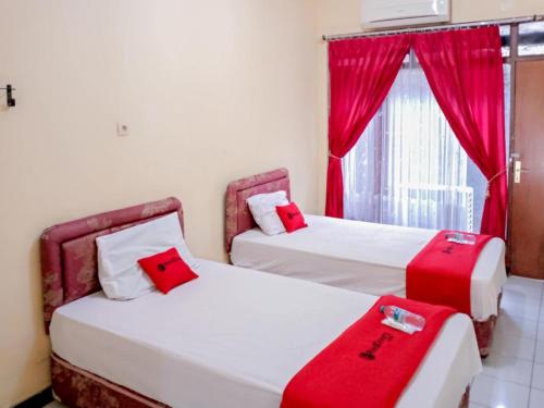 two beds with red pillows in a room with a window at RedDoorz near Politeknik Perkeretaapian Indonesia Madiun in Madiun