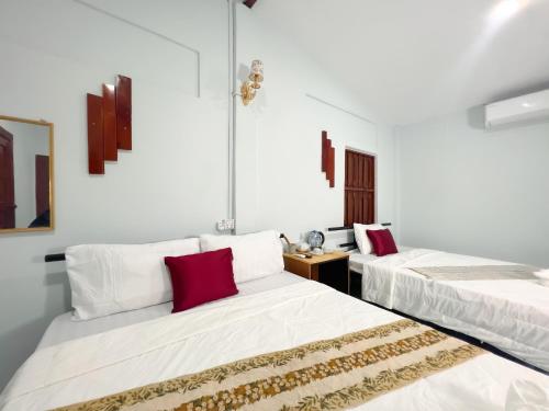 two beds in a room with white walls and red pillows at Lotus Blanc Homestay in Battambang
