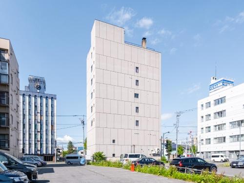 een wit gebouw met auto's geparkeerd op een parkeerplaats bij Tabist THE GREEN ASAHIKAWA in Asahikawa
