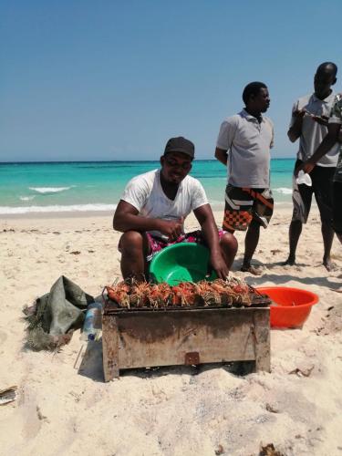 a man sitting on a beach with a container of lobsters at Casa Carlotta & Villa in Nungwi