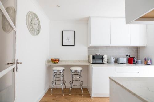 a white kitchen with white cabinets and bar stools at Gorgeous Modern Apartment near Redhill Station inc Private Garden & Parking in Redhill