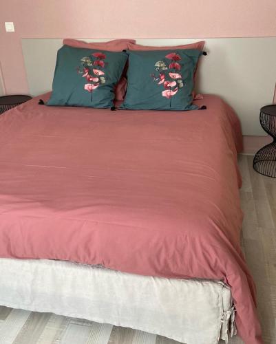 a bed with red sheets and two green pillows at La Rose des vents in Saint-Symphorien-de-Marmagne
