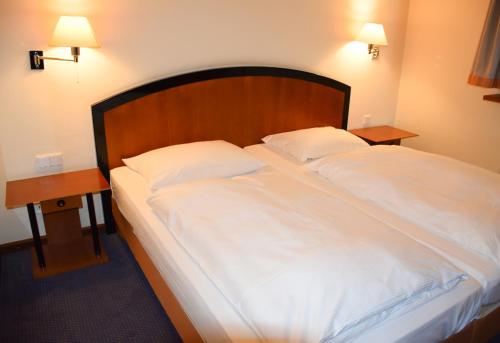City Hotel Dresden Radebeul في راديبول: سرير كبير بملاءات بيضاء وجلستين ليلية