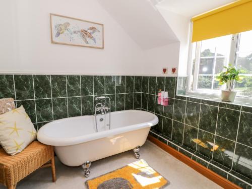 a green tiled bathroom with a tub and a window at Preswylfa in Conwy
