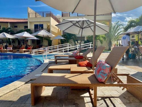 una piscina con sillas y sombrillas junto a una piscina en Flat Solar Água 127 - Family & Friends en Pipa