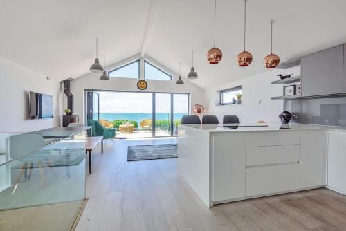 a kitchen with white cabinets and a dining room with the ocean at Seafire Beach House - West Wittering in West Wittering