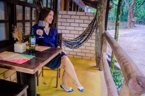 uma mulher sentada à mesa com uma garrafa de vinho em Chalé 03 Itaipu Vale da Colina Niterói em Niterói