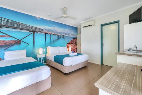 two beds in a room with a painting of a pier at Darwin FreeSpirit Resort in Darwin