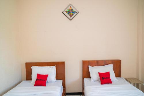 two beds in a room with red pillows at RedDoorz Plus Syariah At Lotus Hotel Bojonegoro in Bojonegoro