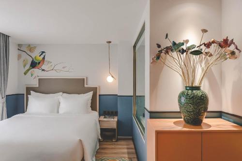 a bedroom with a bed and a vase with flowers on a table at Hanoi Le Jardin Hotel & Spa in Hanoi