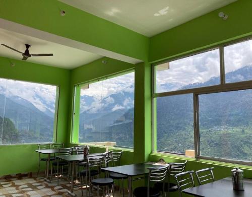 een groene kamer met tafels, stoelen en ramen bij Amardeep Homestay by StayApart in Ukhimath
