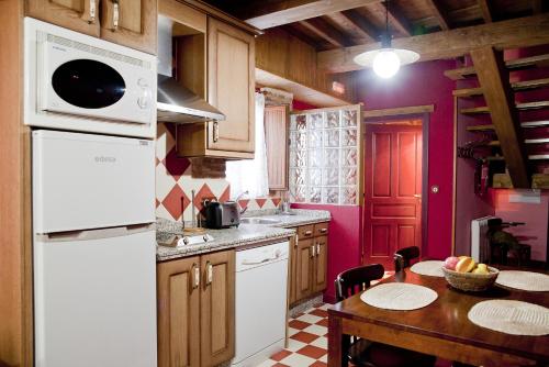 a kitchen with a white refrigerator and a table at CASA RURAL ARBEQUINA, Primavera en el Valle del Ambroz in Casas del Monte