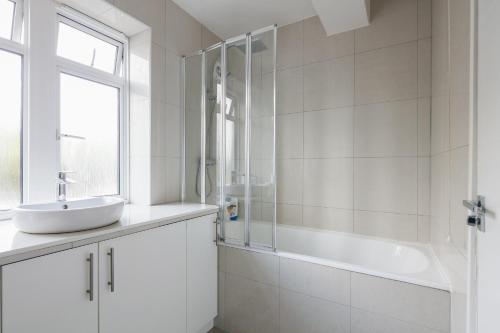 a white bathroom with a sink and a tub at Bright & welcoming garden flat sleeps 6 in style in London