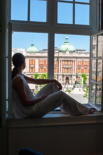 a woman sitting in a window looking out at a building at Hotel Centar No.1 in Belgrade
