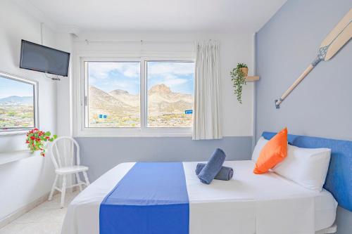 a white and blue bedroom with a bed and a window at Hostel Neon Tenerife in Guaza