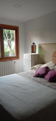 a bedroom with a bed with purple pillows and a window at Acogedora cabaña con piscina in Pontevedra