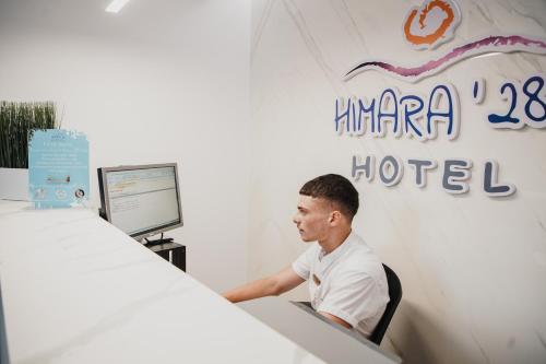 un hombre sentado en un escritorio frente a una computadora en Himara 28 Hotel, en Himare