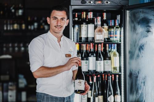 a man holding a bottle of wine in front of a refrigerator at Himara 28 Hotel in Himare