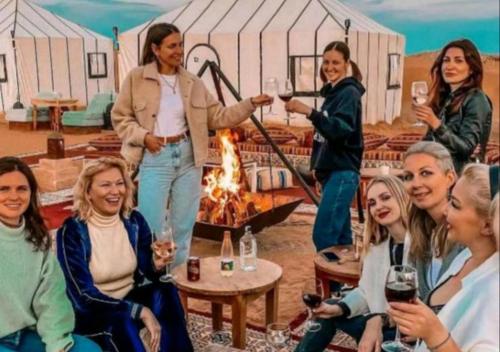 a group of women drinking wine in front of a fire at Fantastic Luxury Camp in Merzouga