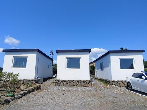 zwei weiße Gebäude mit einem Auto vor ihnen geparkt in der Unterkunft Fongnang Eyeom in Jeju-do