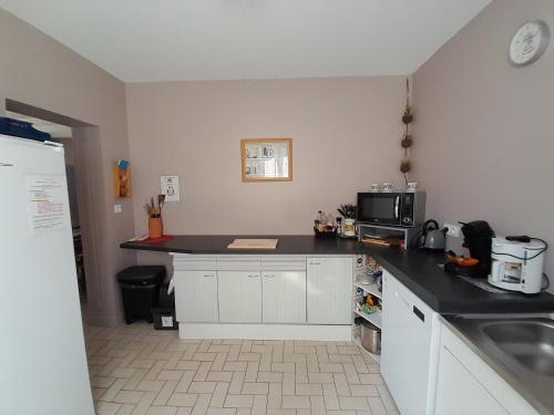 Una cocina con gabinetes blancos y una encimera negra. en Au doux refuge, en Saint-Exupéry-les-Roches