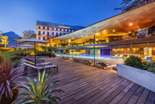 a large building with a deck with benches and umbrellas at Lido Palace - The Leading Hotels of the World in Riva del Garda