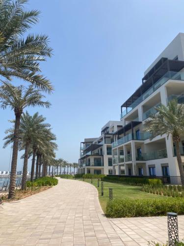a building on the beach with palm trees and a sidewalk at Two Bedroom Apartment Address Residence - Fujairah in Fujairah