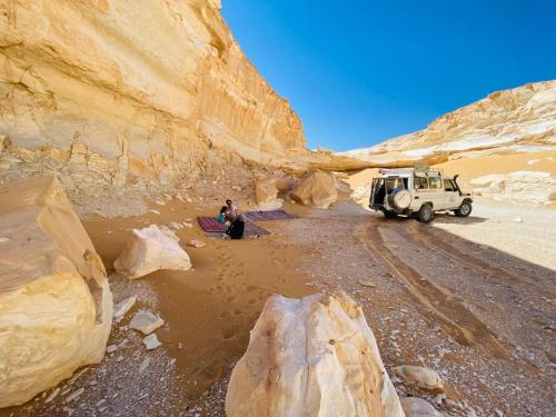 a jeep parked in a desert with a person standing next to it at Rahala Safari Hotel in Qasr Al Farafirah