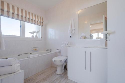 baño blanco con bañera, aseo y lavamanos en Jeffreys Bay Beach Accommodation en Jeffreys Bay