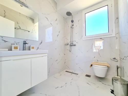 a white bathroom with a toilet and a window at Mythic Seaview Villas in Kiotari