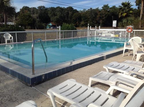 una piscina con sillas blancas y una pista de voleibol en The Suwannee Gables Motel & Marina, en Old Town