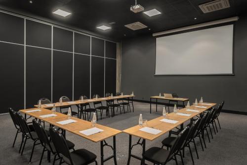 a conference room with tables and chairs and a white screen at Intercity Canoas in Canoas
