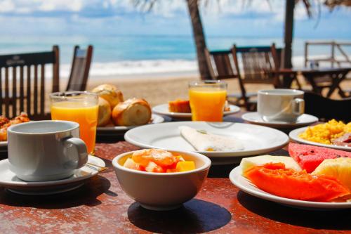 una mesa con platos de comida y bebida en la playa en Pousada Xalés de Maracaípe, en Porto de Galinhas
