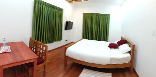 Schlafzimmer mit einem Bett, einem Schreibtisch und grünen Vorhängen in der Unterkunft Moon Homestay in Santhanpara