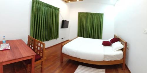 a bedroom with a bed and a desk and green curtains at Moon Homestay in Santhanpara