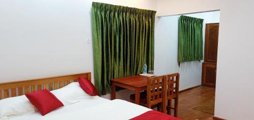 Schlafzimmer mit einem Bett und einem Tisch sowie grünen Vorhängen in der Unterkunft Moon Homestay in Santhanpara