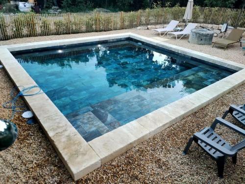 uma piscina num quintal com duas cadeiras de jardim em Le petit écureuil em Saint-Saturnin-dʼApt