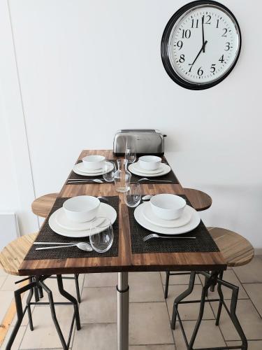 a wooden table with plates and glasses and a clock at Appart confort#1, centre-ville, Gare à pieds proche commodités in Maubeuge