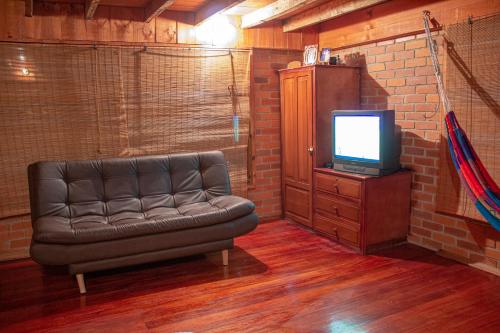 a living room with a leather couch and a tv at Laguna de la Cocha - Cabaña Janaxpacha in Los Alisales