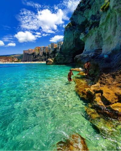 two people walking in the water next to a cliff at Caia Appartamenti Tropea in Tropea